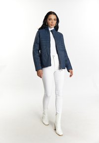 Giacca trapuntata blu navy con collo alto, chiusura a zip e maniche lunghe, abbinata a jeans skinny bianchi e stivali alla caviglia bianchi lucidi.