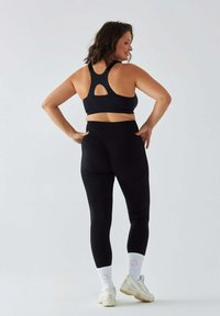 Czarny sportowy biustonosz z wycięciem typu racerback, zestawiony z czarnymi legginsami z wysokim stanem. Jasne buty sportowe i białe skarpetki z różowym serduszkiem.