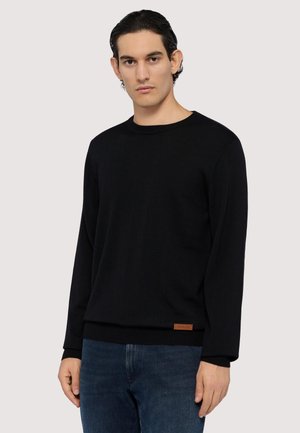 Schwarzer Strickpullover mit rundem Halsausschnitt, gerippten Bündchen und Saum. Mit einem kleinen braunen Lederlogopatch an der Seite.