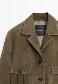 Olivgrüne Wildlederjacke mit breitem Kragen, knöpfbarer Vorderseite und Klappentaschen, beschriftet mit Massimo Dutti, hergestellt in Indien.