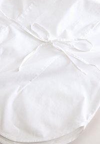 White cotton apron featuring a smooth texture, tied bow at the waist, and a simple, unembellished design suitable for kitchen use.