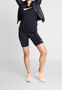Completo sportivo nero composto da una canotta traspirante e pantaloni corti attillati, abbinato a scarpe da corsa rosa chiaro. Accenti del logo del brand in argento.