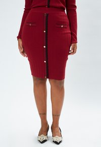 Gerippter burgunderfarbener Bleistiftrock mit goldfarbener Knopfverschluss vorne, schwarzem gewelltem Saum und zwei seitlichen Taschen mit goldenen Akzenten.