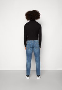 Suéter negro de cuello alto, jeans de denim azul y zapatillas blancas. Los jeans presentan un corte clásico con bolsillos traseros, diseño ajustado y un ligero desgastado.