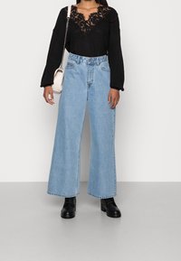 Wide-leg blue denim jeans paired with a black knitted top featuring a lace design on the neckline. Accessories include a small white bag.