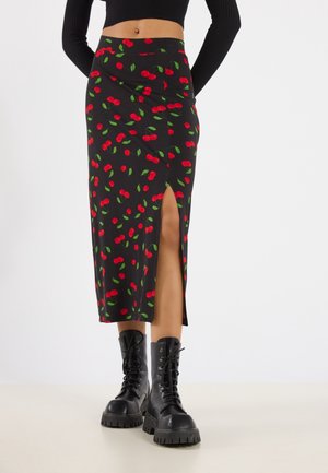 Zwarte midirok met rode kersenprint en een zijsplit, gedragen met zwarte vetercombatlaarzen en een cropped zwart geribd topje.