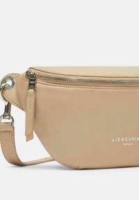 Vaaleanbeige nahkainen laukku, jossa on pyöreä muoto, hopeavetoketju ja logoyksityiskohta. Varustettu säädettävällä hihnalla monipuolisuutta varten.