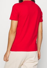 Červené tričko s krátkým rukávem vyrobené z bavlny, s klasickým kulatým výstřihem a standardním střihem. Hladký povrch s minimálně viditelnými švy.