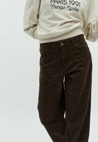Braun gestreifte Hose aus weichem Stoff, mit Knopfverschluss, Gürtelschlaufen und seitlichen Taschen.