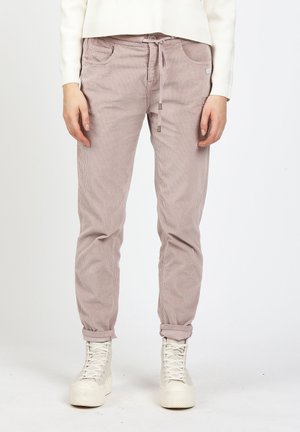 Person wearing light pink corduroy pants with drawstring waist and white high-top sneakers, standing against white background.