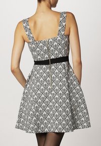 Abito a fantasia bianco e nero con corpetto aderente, gonna svasata, scollatura quadrata e una cintura nera in vita. Presenta una cerniera sul retro.