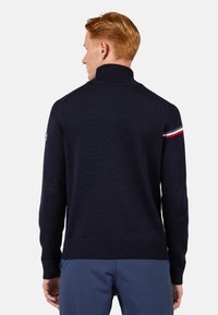 Maglione di maglia navy con colletto alto, polsini e orlo a coste. Presenta strisce rosse, bianche e blu sulla manica sinistra. Vestibilità classica.