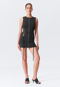 Zwarte mini-jurk met mouwloos ontwerp, voorzien van vetersluitingen aan de zijkanten en metalen oogjes, gestructureerde stof en verstelbare trekkoorden.