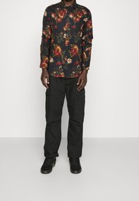 Blommig skjorta med knappar som har en svart bakgrund, stora röda och gula blommor, tillsammans med svarta cargobyxor och svarta sneakers.