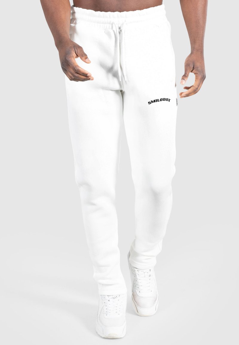 Hvide sweatpants med elastisk talje og sort "SMILODOX" logo på venstre lår, med en glat, blød tekstur.