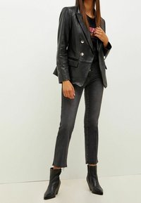 Kvinna iklädd svart läderjacka med dubbla knäppningar, svarta avkortade jeans med fransade fållar, svarta spetsiga ankelstövlar och en skjorta med paljetter i randigt mönster.