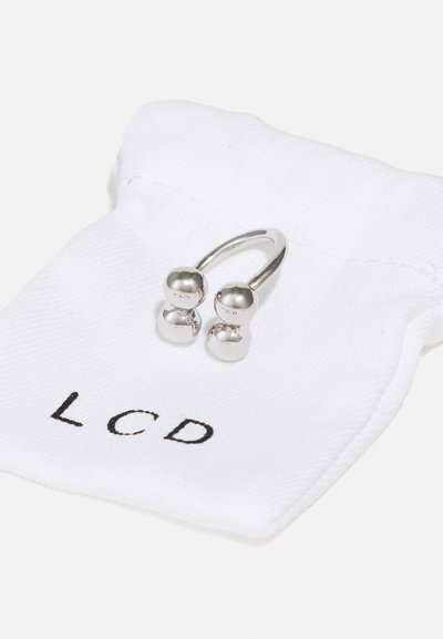 Silver earrings featuring two rounded balls on a curved band, resting on a white fabric pouch with "LCD" printed in black.