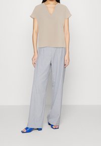 Blusa beige a V con maniche corte abbinata a pantaloni palazzo grigio chiaro e sandali azzurri con tacco a blocco.