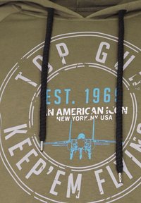 Olivgrön hoodie med svarta snoddar. Har vita och blå tryckta grafik, inklusive ett flygplan och text, på framsidan.