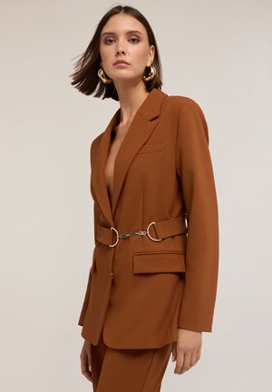 Blazer marrone con un design strutturato, caratterizzato da una tasca singola, una cintura con anelli metallici e un colletto a punta. Tessuto liscio, vestibilità sartoriale.