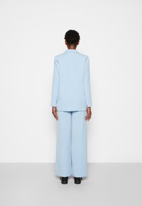 Traje ajustado de color azul claro con un blazer largo y pantalones de pierna ancha, que presenta una textura suave y acentos mínimos, visto desde la parte de atrás.