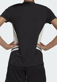 Camisa atlética negra de manga corta, con paneles laterales blancos y franjas blancas horizontales en el dobladillo. Tela suave y ligera.