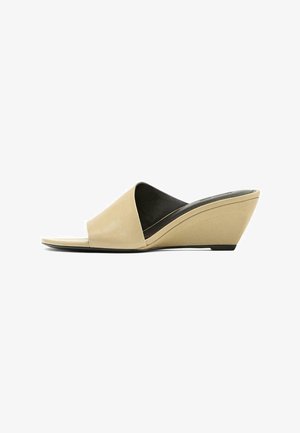 Beżowy sandał na koturnie z odkrytymi palcami, szerokim paskiem i czarną wyściełaną wkładką, na białym tle.