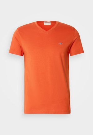 T-shirt in cotone arancione con scollo a V, maniche corte e un piccolo logo sul petto. Texture liscia e cuciture uniformi.