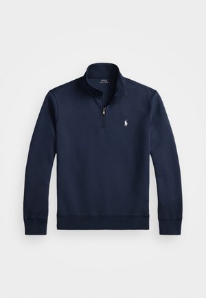 Pull-over bleu marine avec un zip quart, fabriqué dans un tissu lisse. Il présente un petit logo blanc sur la poitrine et des poignets côtelés.