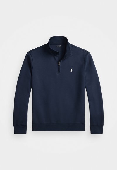 Marineblå pullover sweater med en kvart lynlås, lavet af et glat stof. Har et lille hvidt logo på brystet og ribbede manchetter.