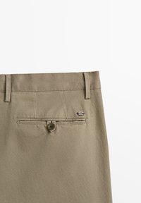 Khaki broek in een gemêleerde katoenen mix. Heeft een achterzak met knoopsluiting en een klein merklabel nabij de tailleband.