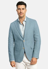 Blazer de lino azul claro con dos bolsillos frontales y cierre de un solo botón. Llevado sobre una camisa con estampado floral.
