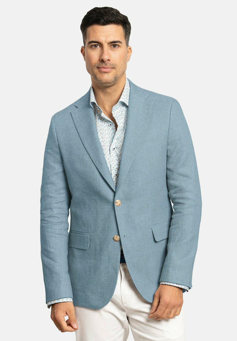 Blazer de lino azul claro con dos bolsillos frontales y cierre de un solo botón. Llevado sobre una camisa con estampado floral.