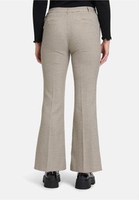 Beige flared broeken met een gestructureerd ruitpatroon, met achterzakken en een middelhoge tailleband. Gecombineerd met zwarte chunky schoenen.