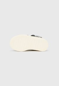 Παπούτσι με λαστιχένια σόλα σε εκρού χρώμα και λαβή με υφή, με γκρι επάνω μέρος από απαλό υλικό και κλείσιμο με λουρί Velcro.