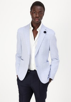 Hellblau strukturierter Blazer mit zwei vorderen Taschen, Ein-Knopf-Verschluss, schwarzer Blumenakzent, getragen über einem weißen Hemd und navyblauen Hosen.