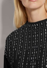 Zwarte kleding met een gestructureerd patroon bestaande uit zilveren rechthoekige en ronde versieringen in verticale strepen over de stof.