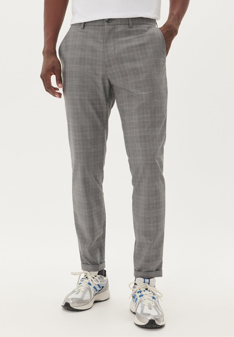 Grå rutiga byxor i lättviktigt tyg, med skräddarsydd passform, snedställda fickor och slät front, kombinerade med sneakers.