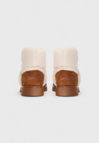 Une paire de bottes en daim marron avec une épaisse doublure en shearling crème et un revers replié, vues de l'arrière sur fond blanc.