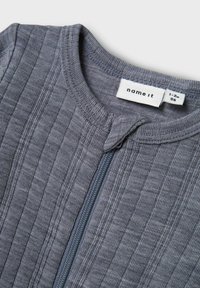 Grå zip-up plagg med vertikal ribbad textur. Har rundad halsringning och varumärkesetikett, lämplig för storlek 1-2 år.