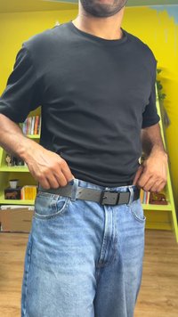 Μαύρο μπλουζάκι και ανοιχτό μπλε τζιν παντελόνι, με μαύρη ζώνη με αγκράφα. Εστίαση στο σώμα και την περιοχή της μέσης με απλό φόντο.