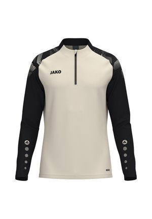 Langærmet sportstrøje med beige front, sorte ærmer, kort lynlås ved halsen, JAKO-logo på brystet og cirkulære mønstre på de nederste ærmer.