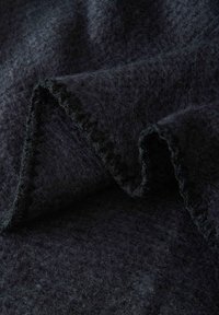 Schwarzer Wollstoff mit einer weichen, strukturierten Oberfläche. Die Ränder weisen eine sichtbare Nahtdetail auf, die eine Falte erzeugt und die Dicke sowie die Fülle des Stoffes betont.