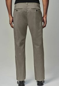 Helle graue Hose aus weichem Stoff mit geradem Beinansatz, zwei Gesäßtaschen mit Knöpfen und sichtbaren Nähten entlang der Nähte.