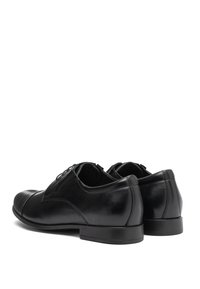 Scarpe da uomo in pelle nera con finitura liscia, punta arrotondata e cuciture minime. Presentano un tacco basso e dettagli di allacciatura nella parte frontale.