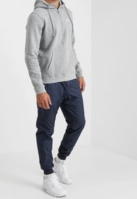 Grå fleece zip-up hoodie med framficka, i kombination med marinblå tapered byxor och vita sneakers. Hoodien har dragsko och logotyp.