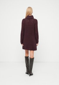 Strikket dyp burgunderkjole med en ribbestrikket krage, som har et strukturert mønster og lange ermer, kombinert med knelang mørkegrå støvler.