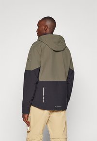 Herren Kapuzenjacke in Olivgrün und Dunkelblau. Verfügt über eine glatte Textur, kontrastierende Farbblöcke und ein reflektierendes Logo-Detail am Saum.