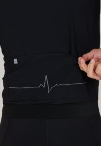 Schwarzes Sportoberteil mit einem Herzschlag-Motiv auf der Rückentasche, ausgestattet mit einem flexiblen Bund und einem glatten, strukturierten Stoff.