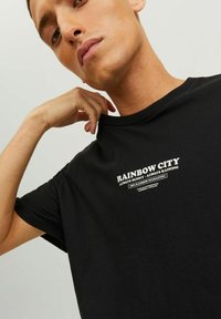 Must musta t-särk, millel on lühikesed varrukad, esiküljel valge graafiline print, mis ütleb "RAINBOW CITY ALWAYS SUNNY · ALWAYS RAINING".